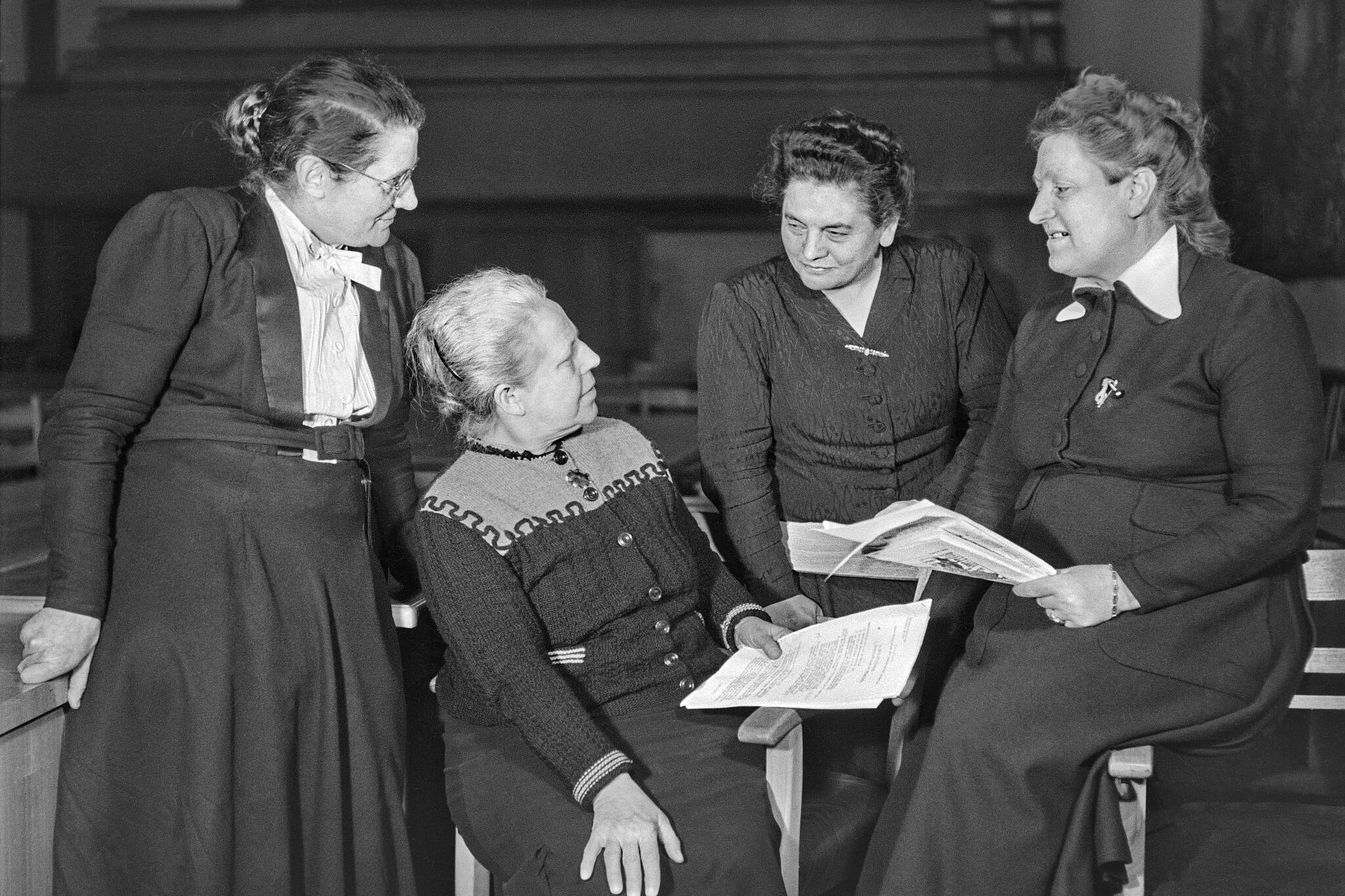 Helene Wessel, Helene Weber, Friederike Nadig und Elisabeth Selbert sitzen und stehen zusammen und sehen sich an.