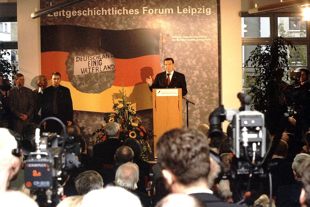 Gerhard Schröder am Rednerpult, dahinter ein großes Plakat mit der Aufschrift Zeitgeschichtliches Forum Leipzig, vor ihm Besucher und Pressevertreter