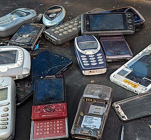 Foto von mehreren alten Handys und Smartphones, teilweise zerstört oder kaputt