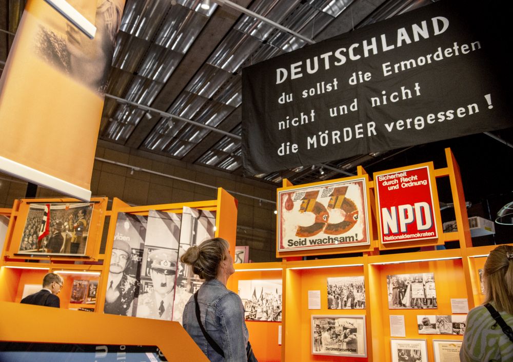 A visitor looks at a black and white banner that reads: Banner ‘Germany you shall not forget the murdered and not the murderers!’