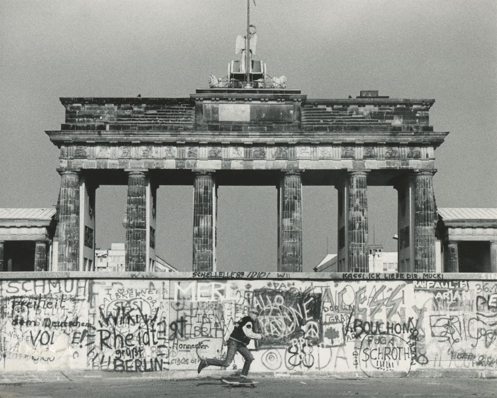 Ein Skater fährt an der Berliner Mauer vorbei mit dem Brandenburger Tor im Hintergrund.