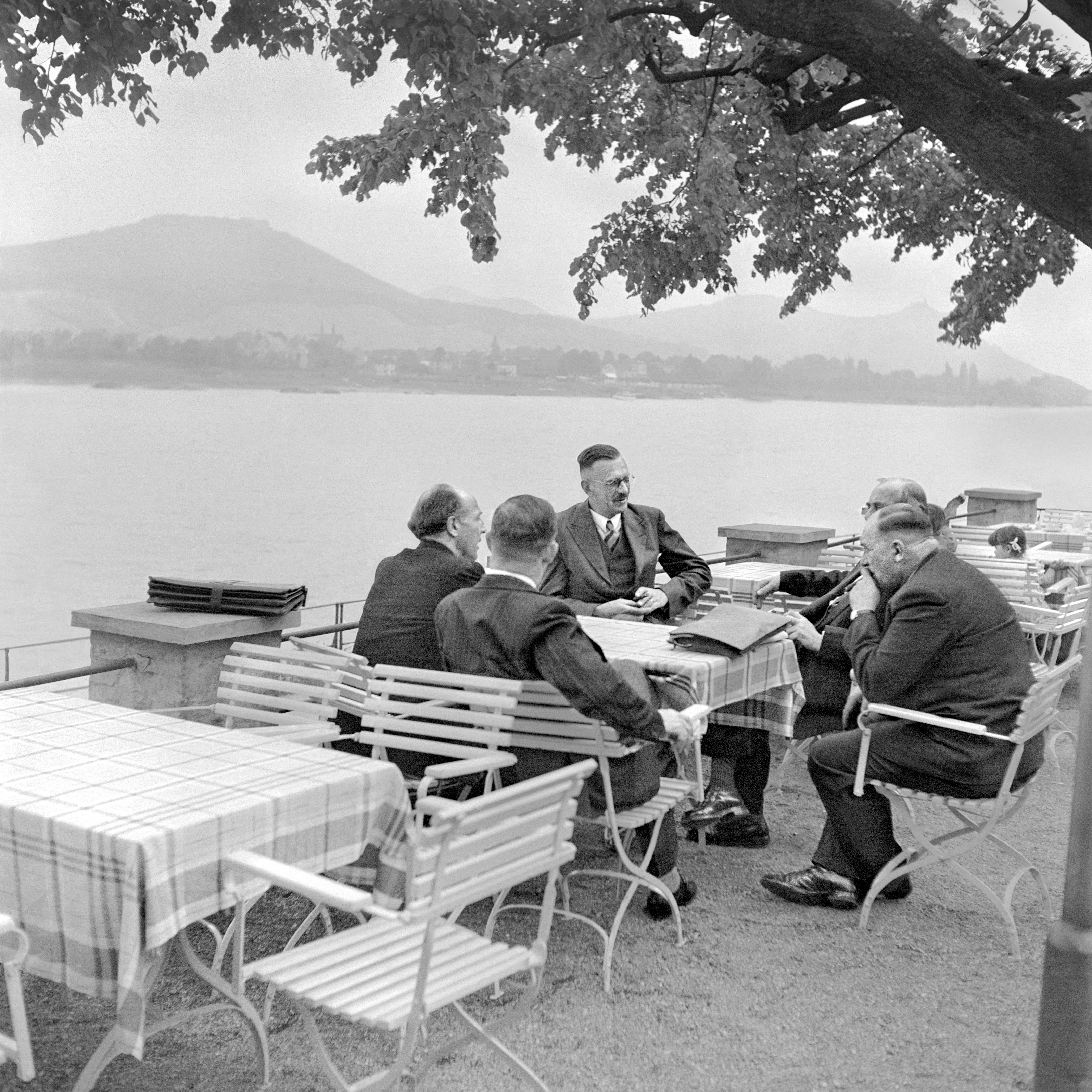 Auf dem historischen Foto sitzen fünf Männer in anzügen in einem Biergarten am Bonner Rheinufer.